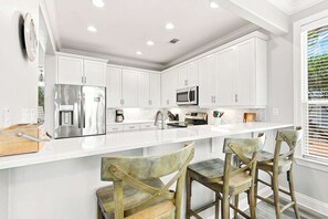 A modern kitchen with white cabinetry, stainless steel appliances, and a central island with bar stools. - Poolside Paradise - Access To Pool, Walk To Beach! (Rosemary Beach)