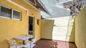 Ein kleiner Patio-Bereich mit Tisch und Stühlen, eine Tür zu einem Innenraum sowie eine Wand mit strukturierter Oberfläche.