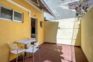 Ein kleiner Patio-Bereich mit Tisch und Stühlen, eine Tür zu einem Innenraum sowie eine Wand mit strukturierter Oberfläche.