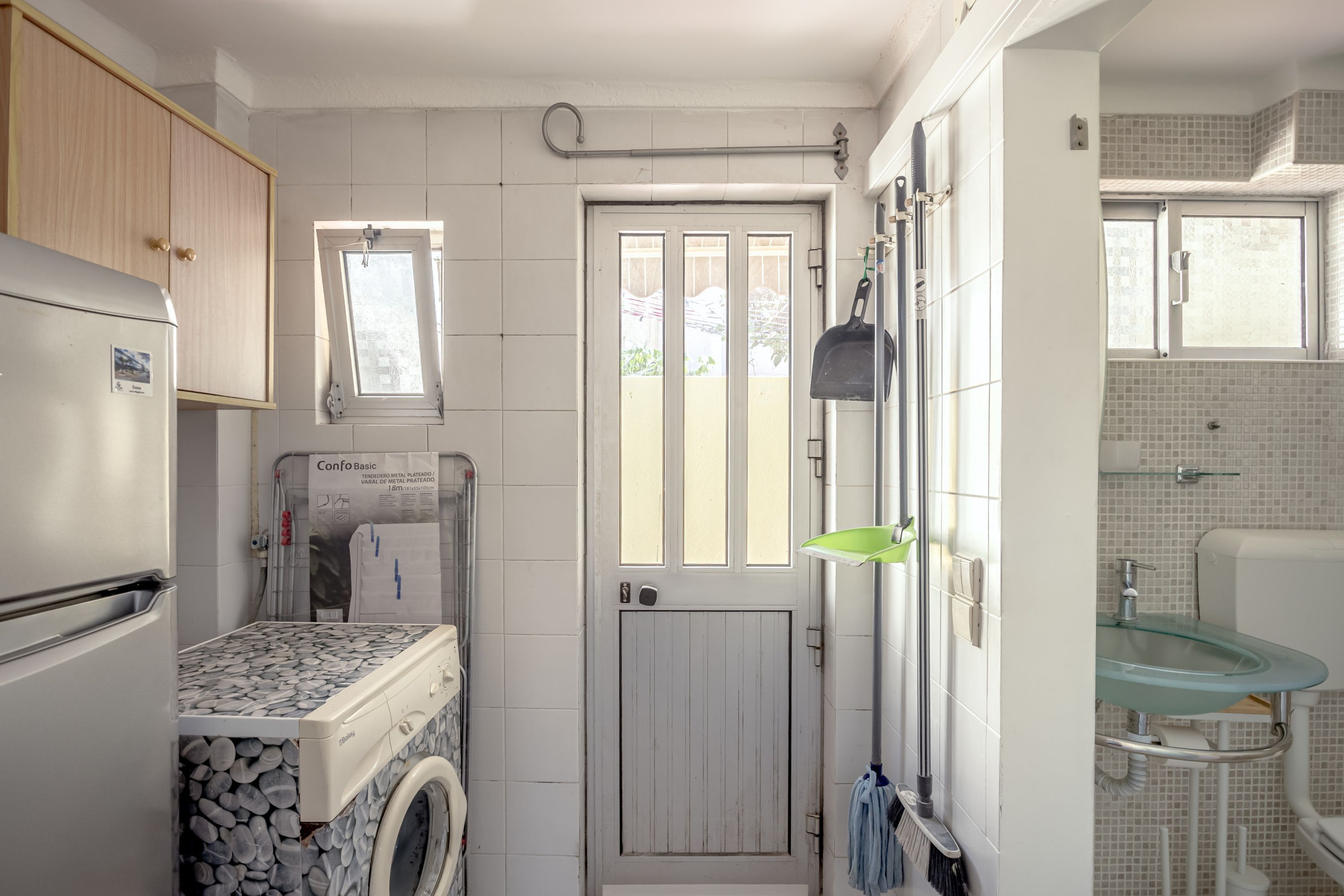 A compact kitchen with a washing machine, a refrigerator, and a window.