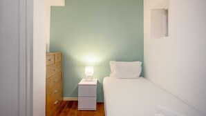 Ein kleines, gut beleuchtetes Schlafzimmer mit einem Einzelbett, einem Nachttisch mit Lampe und einer Holzkombination.