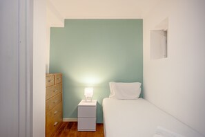 Ein kleines, gut beleuchtetes Schlafzimmer mit einem Einzelbett, einem Nachttisch mit Lampe und einer Holzkombination.