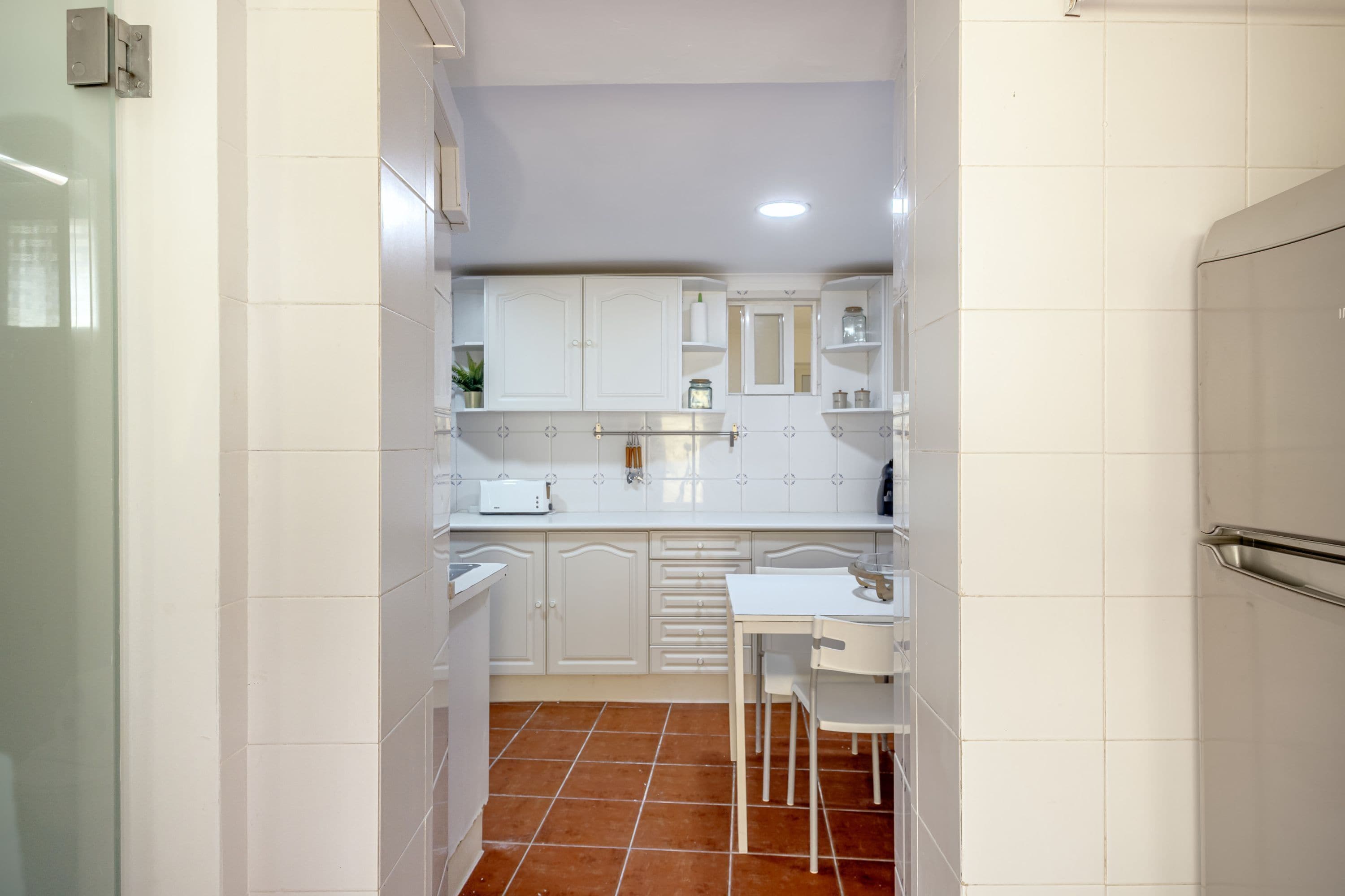 A compact kitchen with white cabinets, a countertop, and a tiled floor.