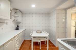 A compact kitchen with white cabinets, a white countertop, a small table with chairs, and a tiled backsplash. - Santana Cosy by Homing (Lisbon)