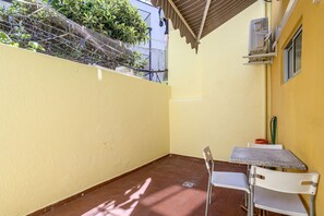 A small patio area with a tiled floor, a white chair, a small table, and an air conditioning unit mounted on the wall. - Santana Cosy by Homing (Lisbon)