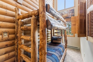 L’intérieur d’une cabane en rondins, avec un lit superposé, des murs en bois et une grande fenêtre.