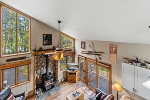 L’intérieur chaleureux d’un chalet avec une cheminée en pierre, des meubles en bois et de grandes fenêtres donnant sur la forêt.