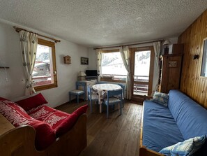 A cozy room with a bed, a sofa, a table with chairs, and a television. - Meribel Mottaret Apartment at the Foot of the Slopes, Sleeps 5, All-Inclusive (Les Allues)