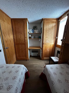 A compact room with two beds, wooden wardrobes, a small desk, and a radiator. - Meribel Mottaret Apartment at the Foot of the Slopes, Sleeps 5, All-Inclusive (Les Allues)
