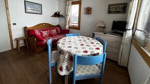 A cozy room with a wooden sofa, a small table, a TV, and a window with curtains. - Meribel Mottaret Apartment at the Foot of the Slopes, Sleeps 5, All-Inclusive (Les Allues)