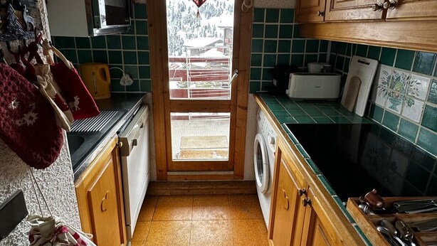 A compact kitchen with a washing machine, a microwave, and wooden cabinets. - Meribel Mottaret Apartment at the Foot of the Slopes, Sleeps 5, All-Inclusive (Les Allues)
