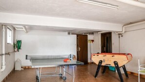 Una habitación con mesa de ping pong, mesa de fútbol y una ventana con persianas.