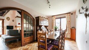 Un comedor con mesa y sillas de madera, suelo con motivo de espiga y un amplio ventanal con cortinas.