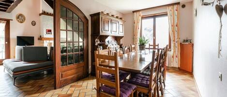 A dining area with a wooden table and chairs, a herringbone-patterned floor, and a large window with curtains.