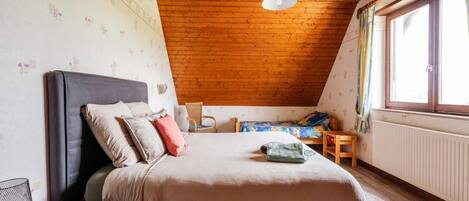 Ein Schlafzimmer mit Holzbalkendecke, einem Bett, einem Fenster und einer Heizung.
