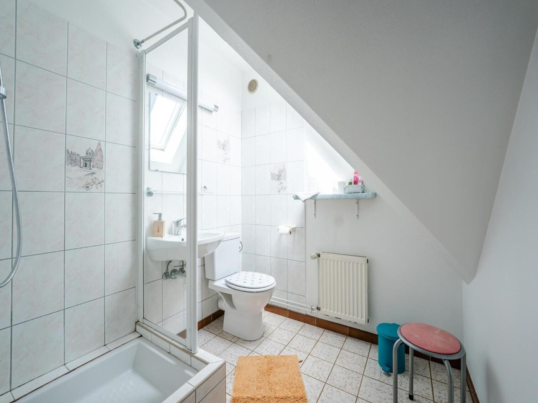 A bathroom with a shower, toilet, and sink, featuring white tiles and a visible skylight.