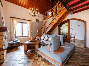 A cozy living room with a sofa, a wooden coffee table, a chandelier, and a staircase.