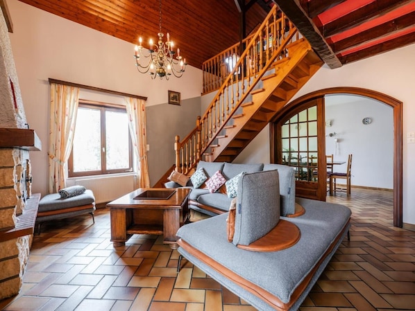 A cozy living room with a sofa, a wooden coffee table, a chandelier, and a staircase.