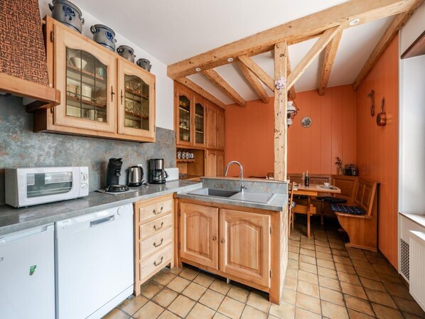 A compact kitchen with wooden cabinets, a built-in dishwasher, and a dining area with a bench.