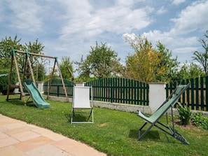 A backyard with a swing set, a slide, a whiteboard, and a green lawn chair.