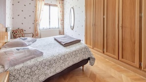 Un dormitorio con cama, armario, espejo y ventana con cortinas.