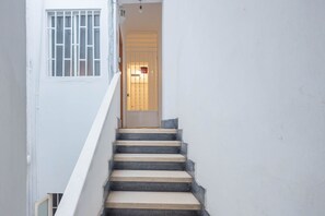 Un escalier menant à une porte surmontée d’une fenêtre grillagée.