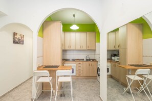 A compact kitchen with wooden cabinets, a sink, and a microwave. There are two white chairs and a small table. - 3-Bedroom Urban Apartment - Central & Comfortable (Las Palmas de Gran Canaria)