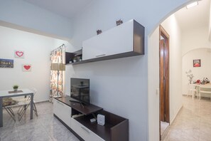 A modern living room with a flat-screen TV, a dining table with chairs, and a kitchen area with a microwave. - 3-Bedroom Urban Apartment - Central & Comfortable (Las Palmas de Gran Canaria)