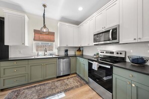 A modern kitchen with white cabinets, a stainless steel dishwasher, a built-in oven, and a microwave. - Apple Street Getaway - Fire Pit & Close to Main St (Fredericksburg)