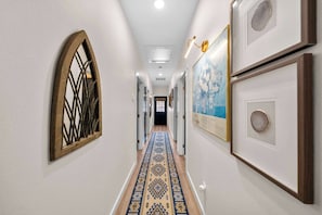 Um corredor com carpete estampado, obras de arte emolduradas e uma porta no final.