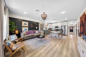 A modern living room with a sofa, coffee table, and a dining area with chairs. - Apple Street Getaway - Fire Pit & Close to Main St (Fredericksburg)