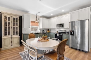 A modern kitchen with white cabinetry, a stainless steel refrigerator, and a round dining table with chairs. - Apple Street Getaway - Fire Pit & Close to Main St (Fredericksburg)
