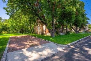A residential street with a driveway leading to a house, surrounded by lush green lawns and mature trees. - The Rustic Door - Hot Tub & 1 Block from Main St (Fredericksburg)