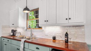 Una cocina con armarios blancos, encimera de madera, ventana con vistas y una botella de vino.