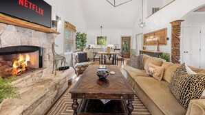Una sala de estar acogedora con chimenea, señal de Netflix, comedor y una lámpara de araña moderna.