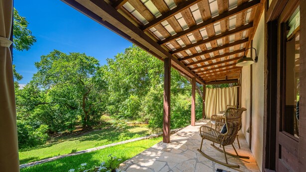 Un patio cubierto con suelo de piedra, una mecedora y vistas a un paisaje verde exuberante.