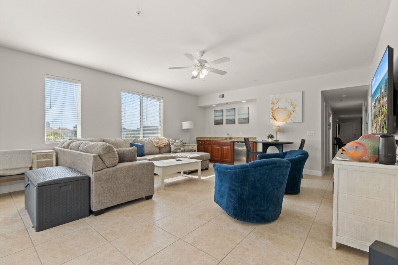 A spacious living area with a sofa, coffee table, and blue armchairs. There is a kitchen area with a dining table and chairs.