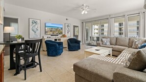 A spacious living room with a sofa, armchairs, a coffee table, and a TV. There is a balcony with a view of the city. - Stunning Golf Spot across from beach, shop, Oceanview, Pool, Elevator (North Myrtle Beach)