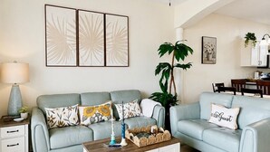 Una sala de estar con ventilador de techo, dos sofás, una mesa de centro y una planta.