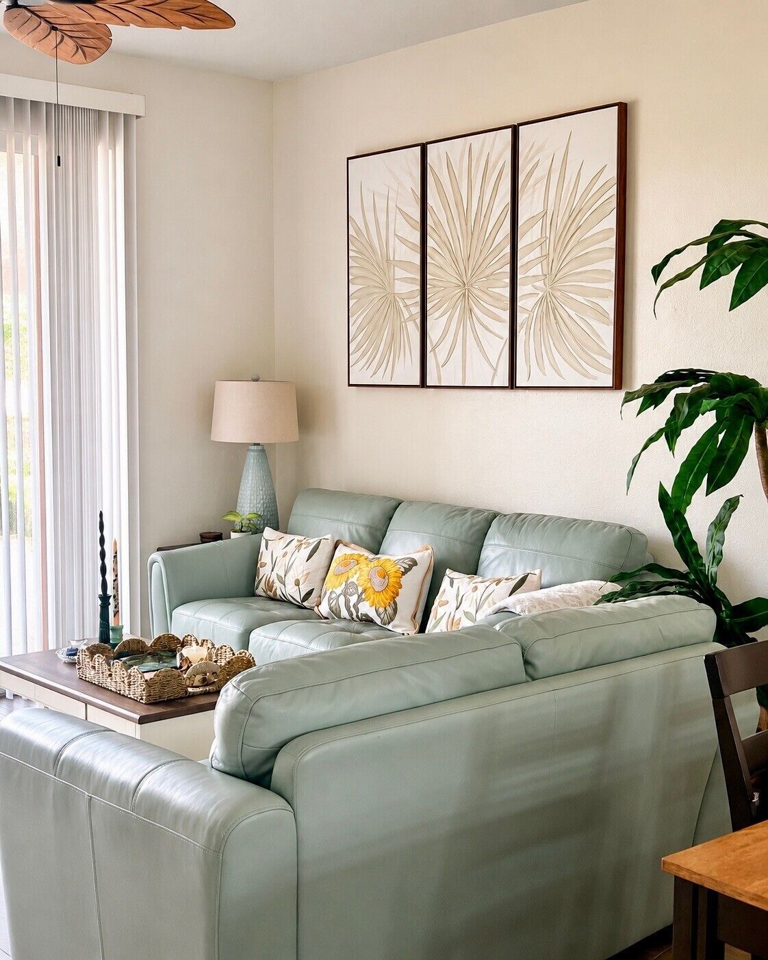 Uma sala de estar com um sofá verde-clarinho, uma mesa lateral com abajur e uma planta grande.