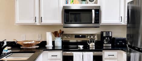 A modern kitchen with white cabinets, stainless steel appliances, a microwave, oven, and a refrigerator.