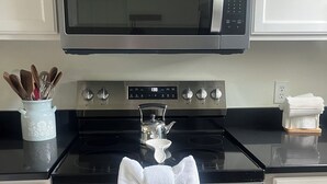 Una cocina con microondas, estufa y horno. Hay libros en el estante encima del microondas.