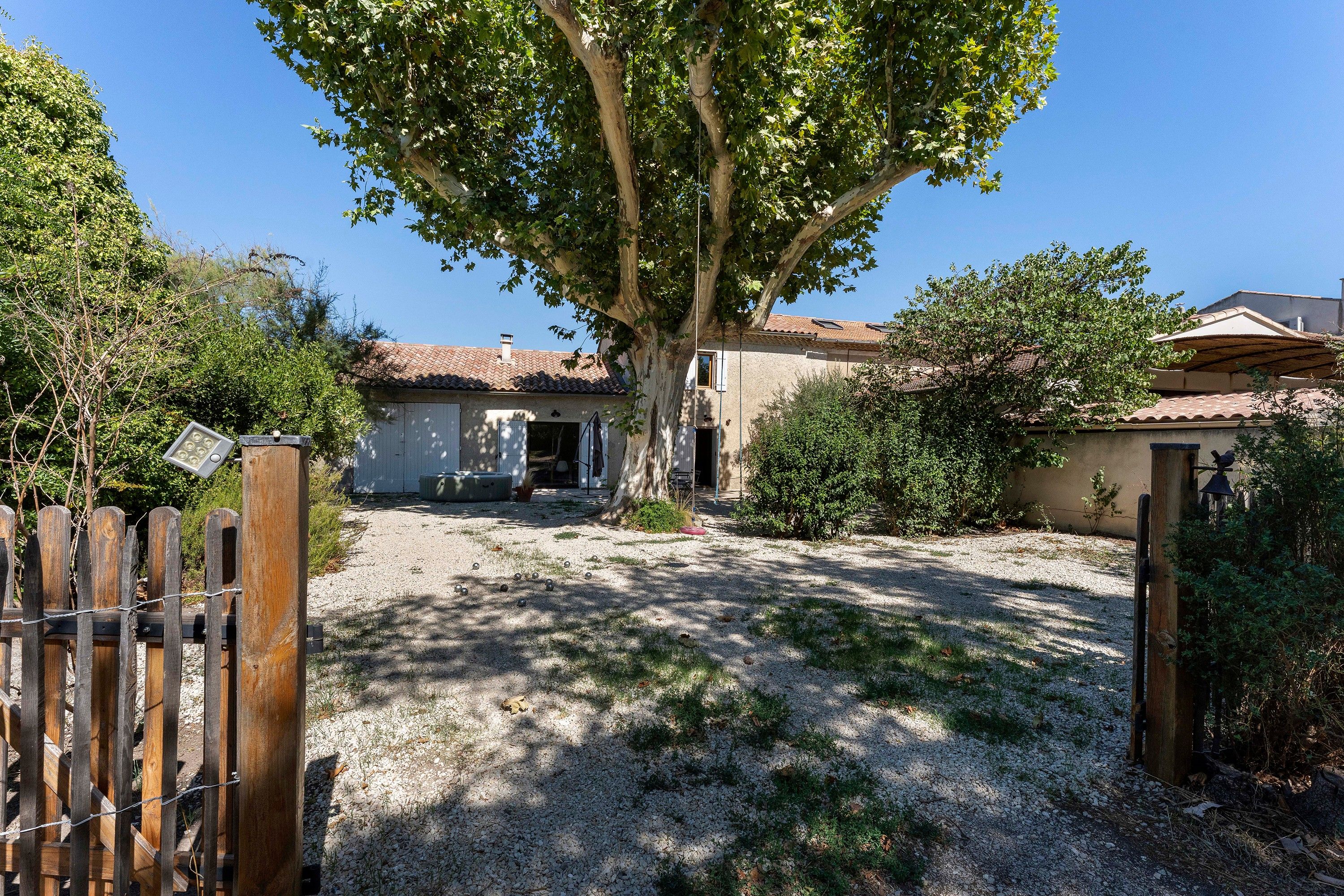 A house with a gravel driveway, a wooden gate, and a tree in the foreground.