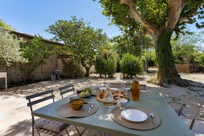 An outdoor dining area with a table set for two, surrounded by trees and a rustic building. - Mas de la Roubine with garden, air conditioning, spa, and Wi-Fi (Châteaurenard)