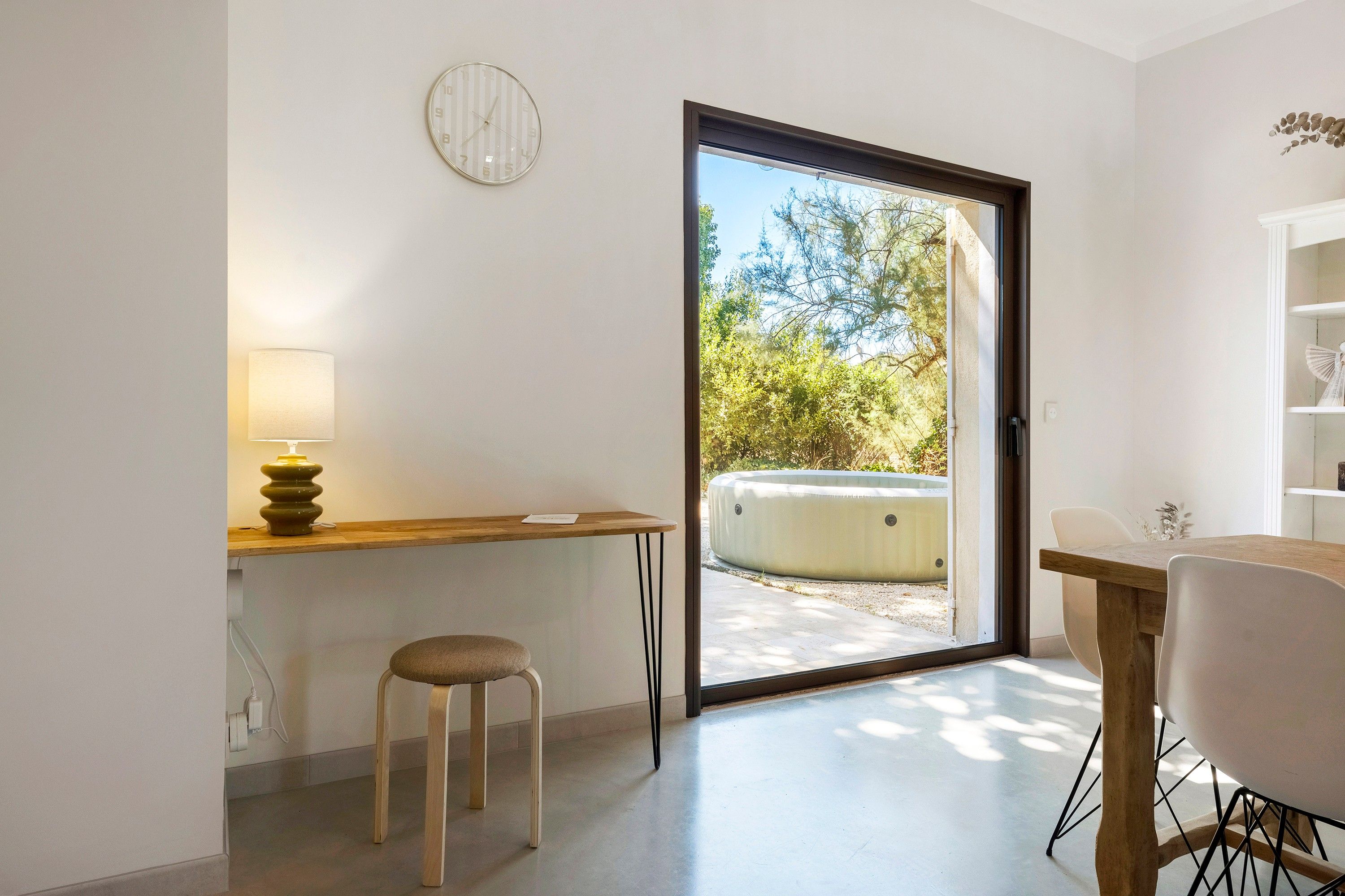 A modern interior with a wooden desk, a chair, a lamp, and a sliding glass door leading to an outdoor area with a hot tub.