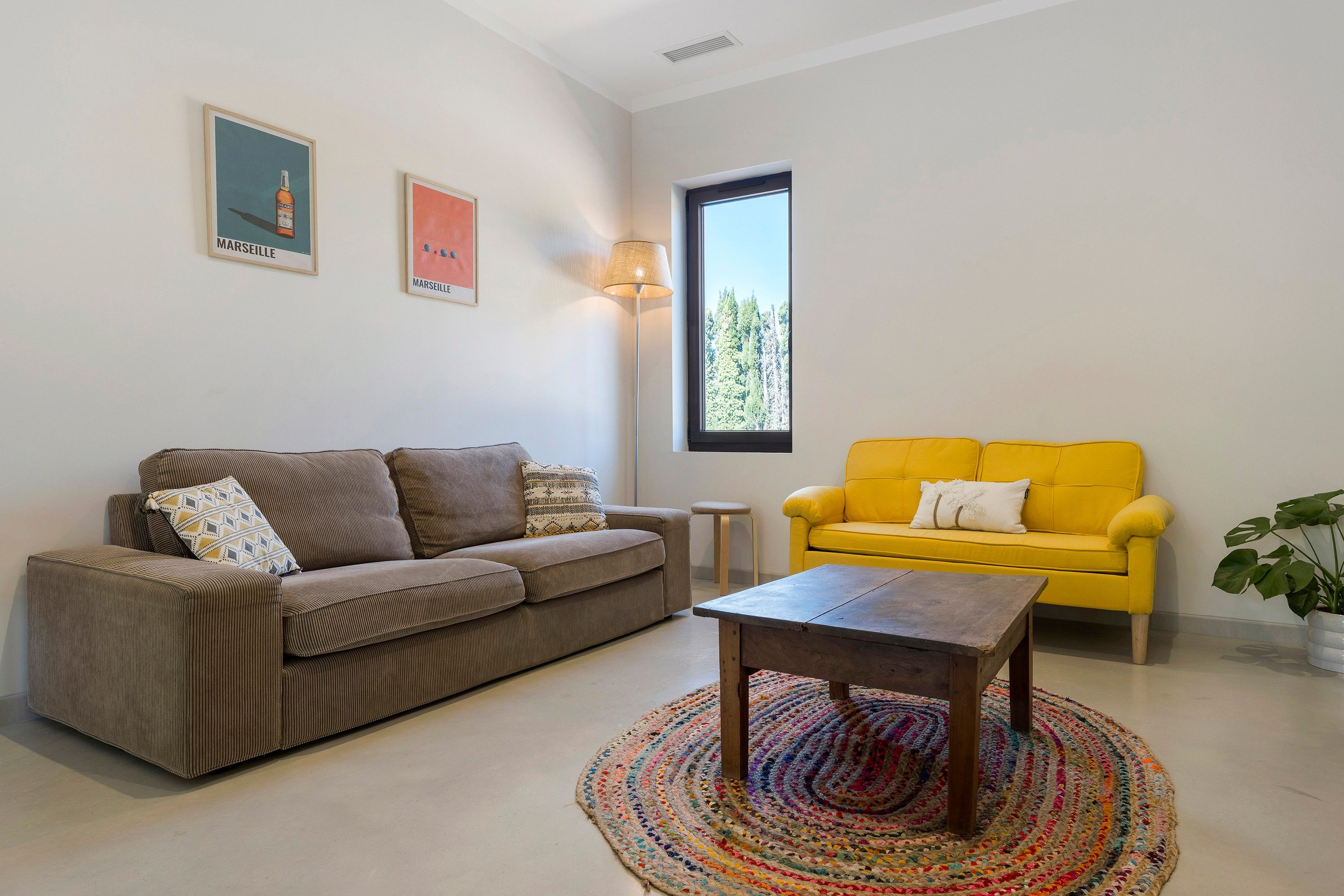 Un salon avec un canapé marron, un canapé jaune, une table basse et un tapis coloré.