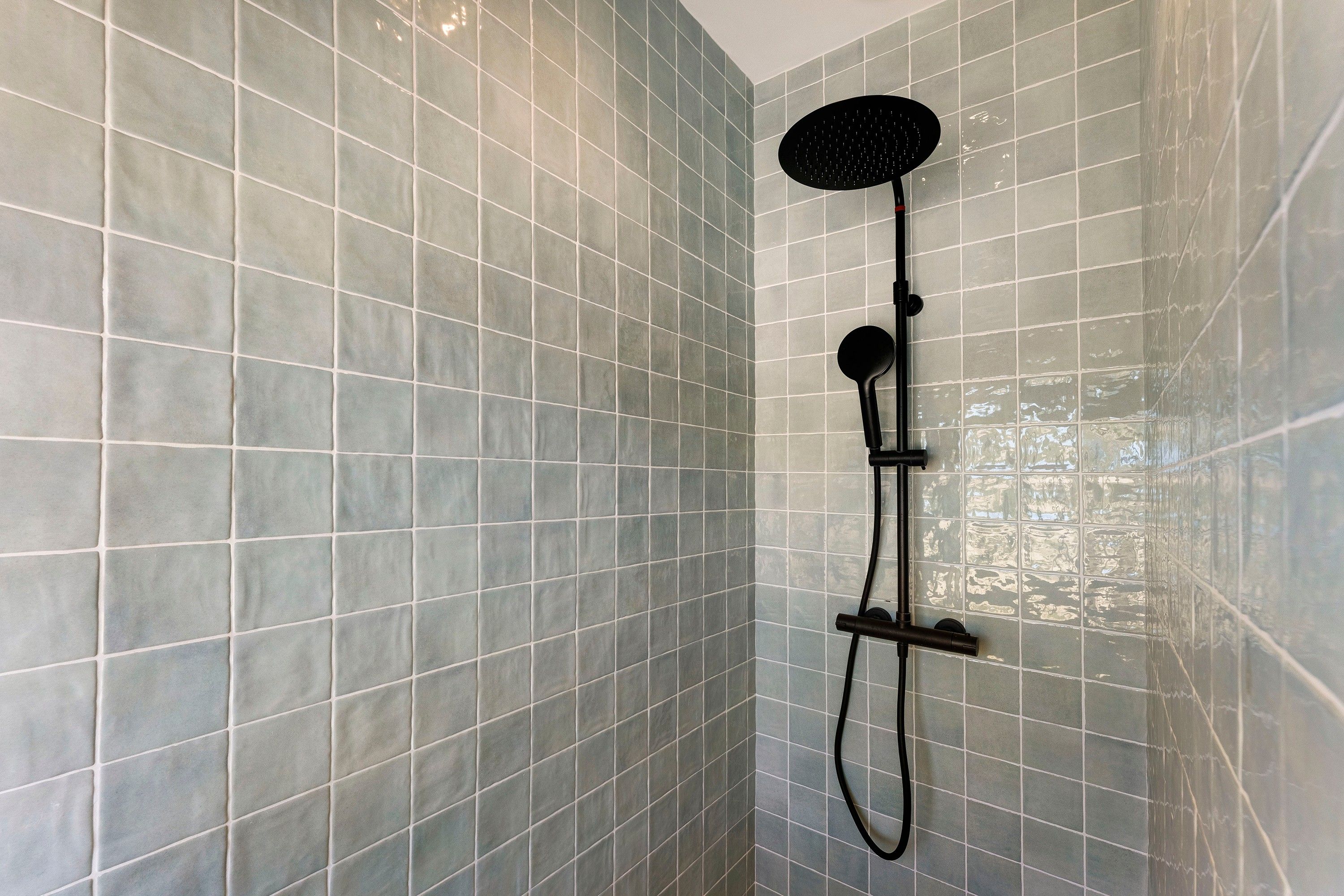 A shower with a handheld showerhead and a wall-mounted control panel.