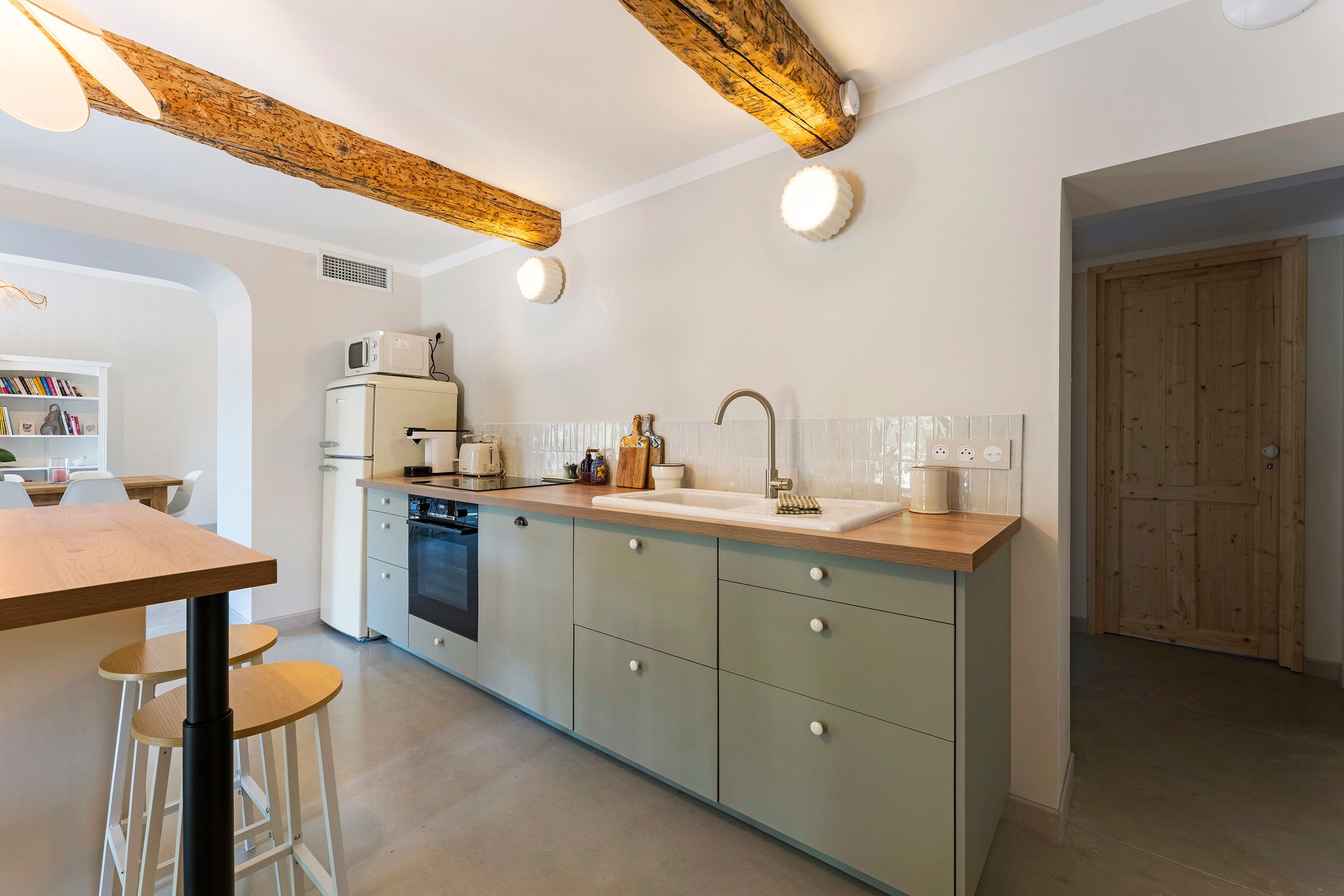 Une cuisine moderne avec un plafond en bois, un four encastré, un évier et un coin repas équipé de tabourets.
