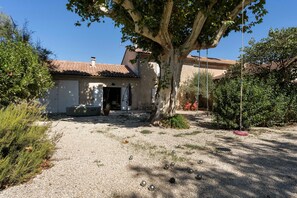 A rustic building with a gravel driveway, a large tree in the foreground, and a clear blue sky. - Mas de la Roubine with garden, air conditioning, spa, and Wi-Fi (Châteaurenard)