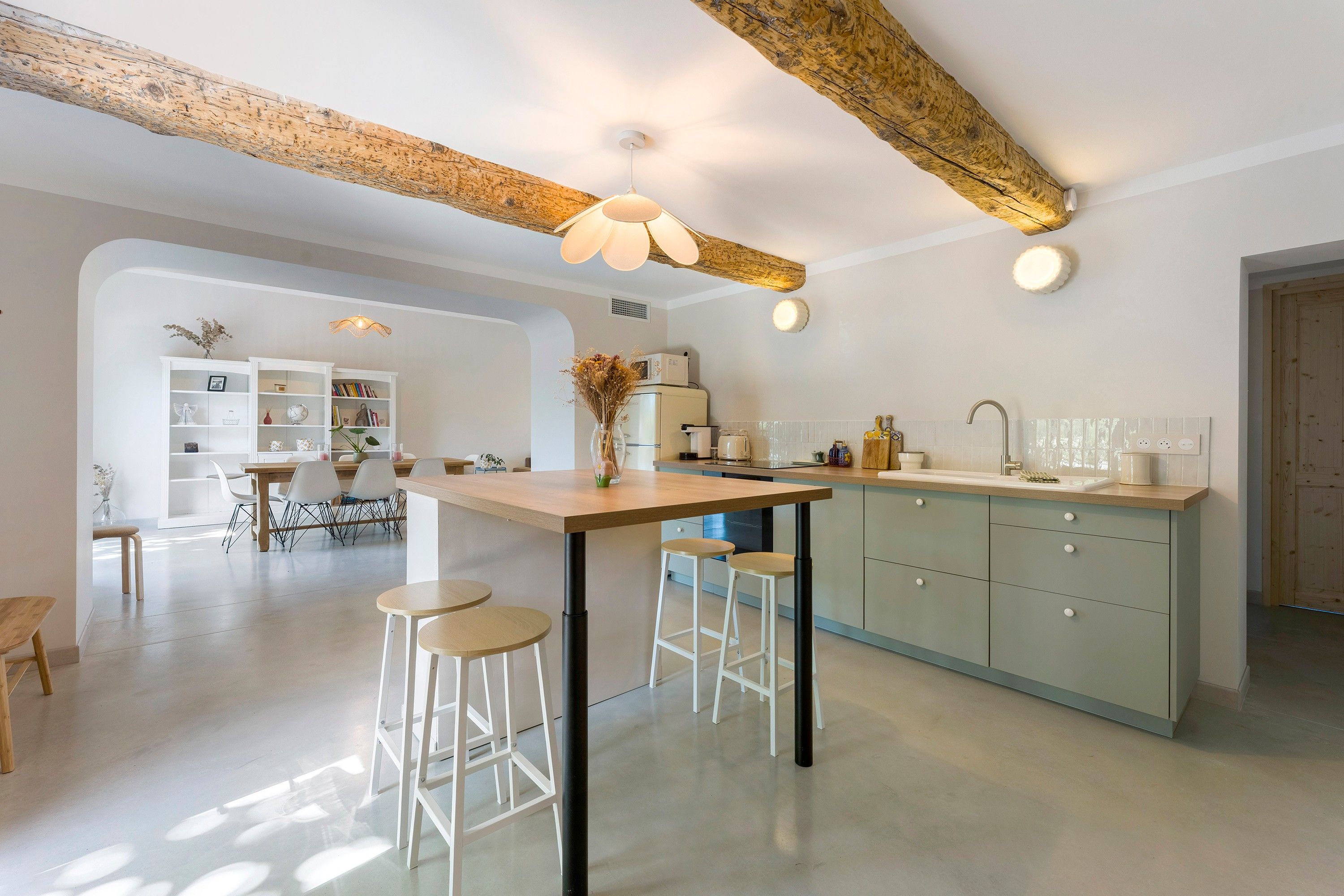 Una cocina moderna con una isla central, taburetes de bar y un comedor con mesa y sillas blancas.